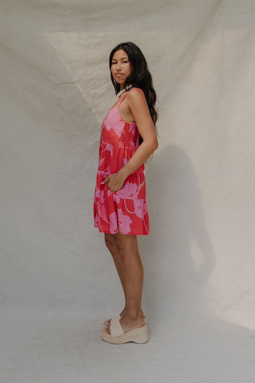 woman with brown hair wearing a red short spaghetti strap dress with pink mao flower pattern