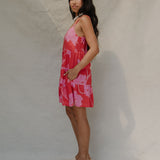 woman with brown hair wearing a red short spaghetti strap dress with pink mao flower pattern