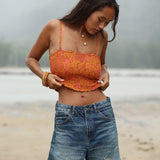 woman with brown hair wearing orange smocked bandeau with removable straps with puakenikeni print