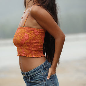 woman with brown hair wearing orange smocked bandeau with removable straps with puakenikeni print