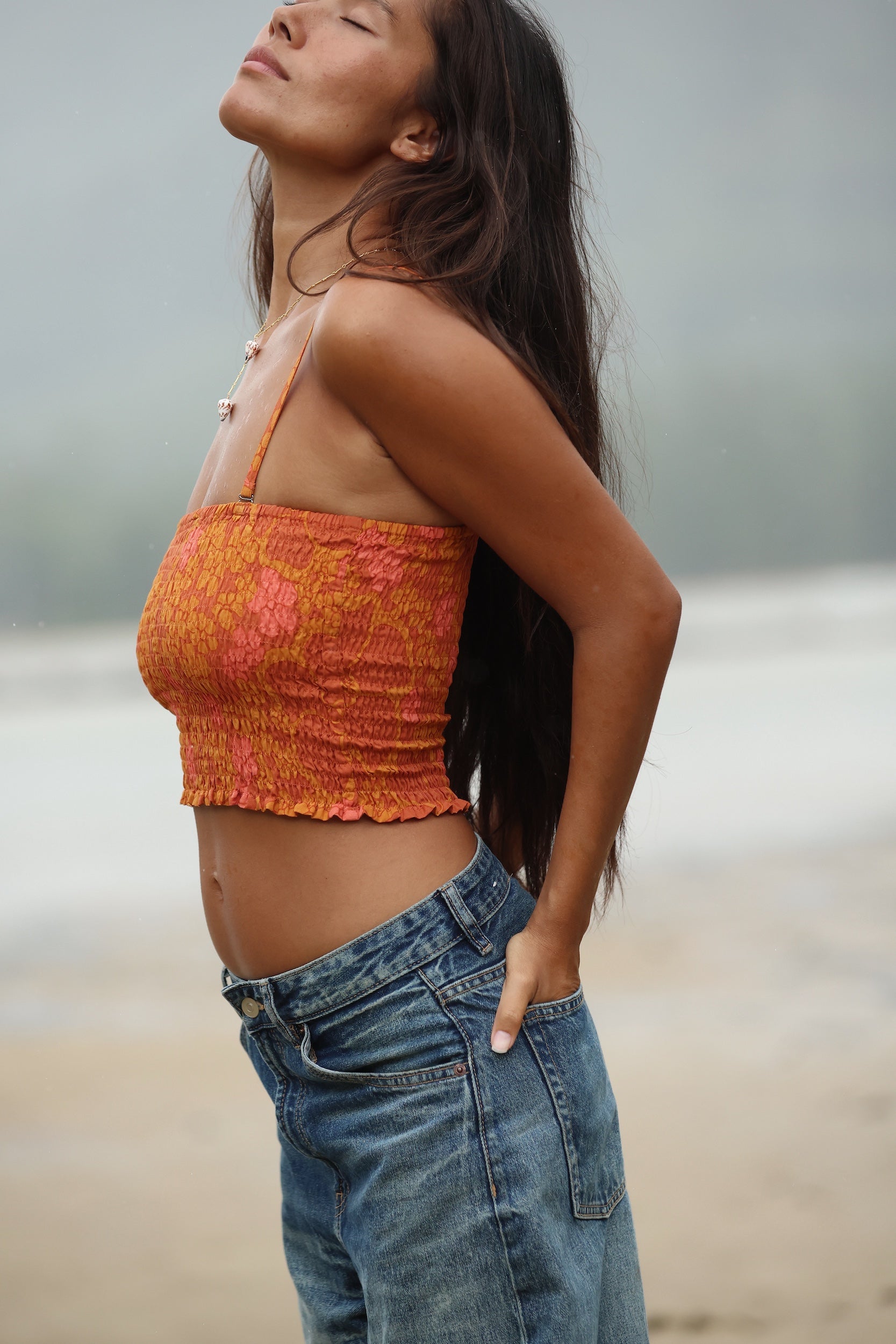 woman with brown hair wearing orange smocked bandeau with removable straps with puakenikeni print