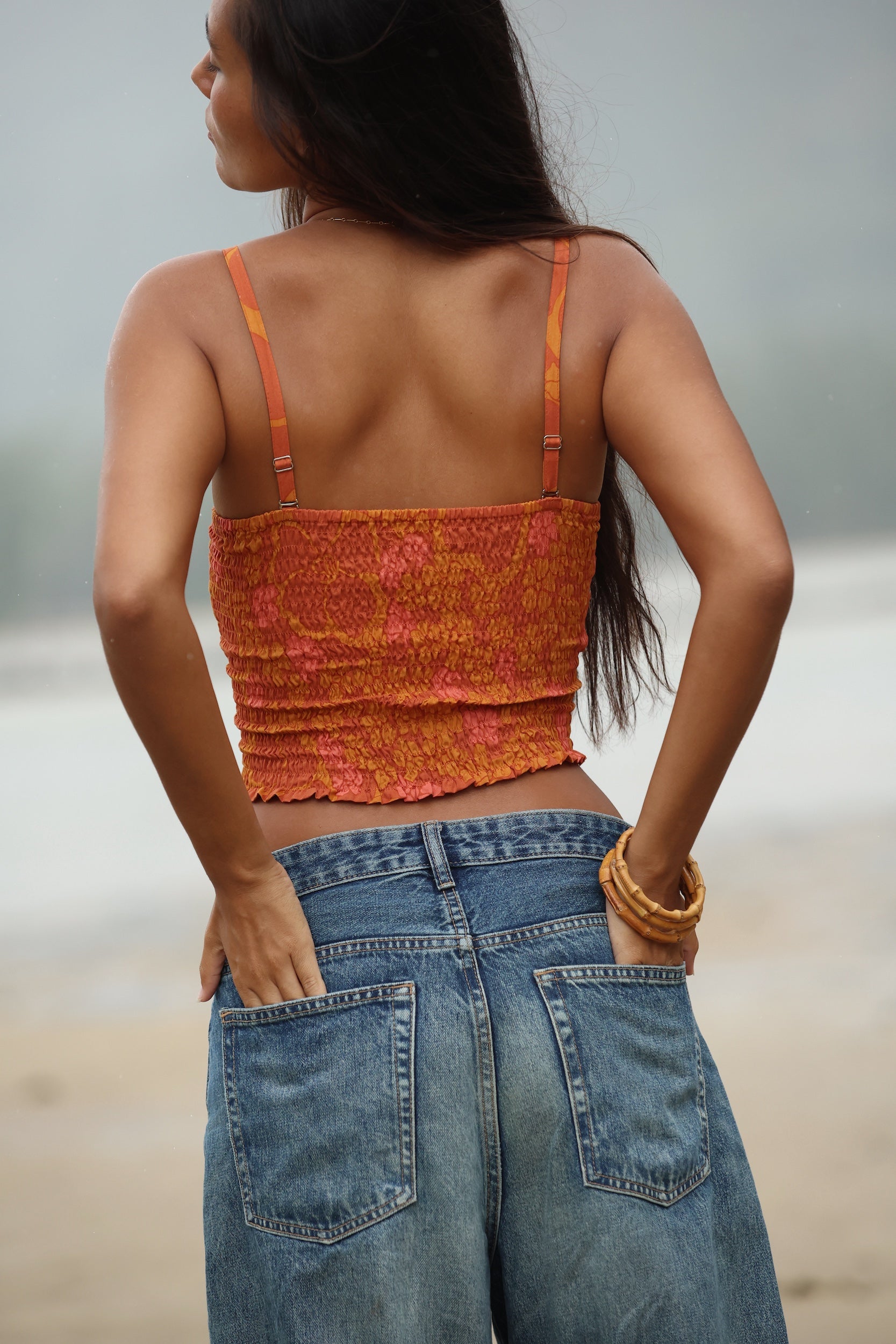 woman with brown hair wearing orange smocked bandeau with removable straps with puakenikeni print