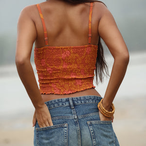 woman with brown hair wearing orange smocked bandeau with removable straps with puakenikeni print