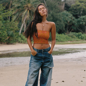 woman with brown hair wearing orange smocked bandeau with removable straps with puakenikeni print