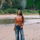 woman with brown hair wearing orange smocked bandeau with removable straps with puakenikeni print