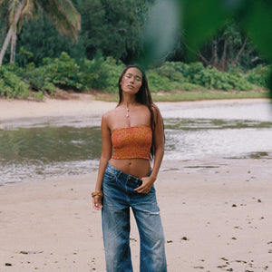 woman with brown hair wearing orange smocked bandeau with removable straps with puakenikeni print