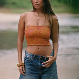 woman with brown hair wearing orange smocked bandeau with removable straps with puakenikeni print