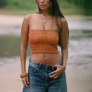 woman with brown hair wearing orange smocked bandeau with removable straps with puakenikeni print
