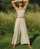 Woman wearing smocked tube top with spaghetti straps and loose pant in beige linen.