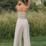 Woman wearing smocked tube top with spaghetti straps and loose pant in beige linen.
