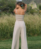 Woman wearing smocked tube top with spaghetti straps and loose pant in beige linen.