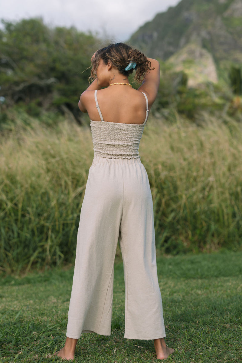 Woman wearing smocked tube top with spaghetti straps and loose pant in beige linen.