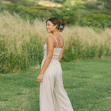 Woman wearing smocked tube top with spaghetti straps and loose pant in beige linen.