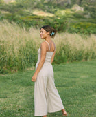 Woman wearing smocked tube top with spaghetti straps and loose pant in beige linen.