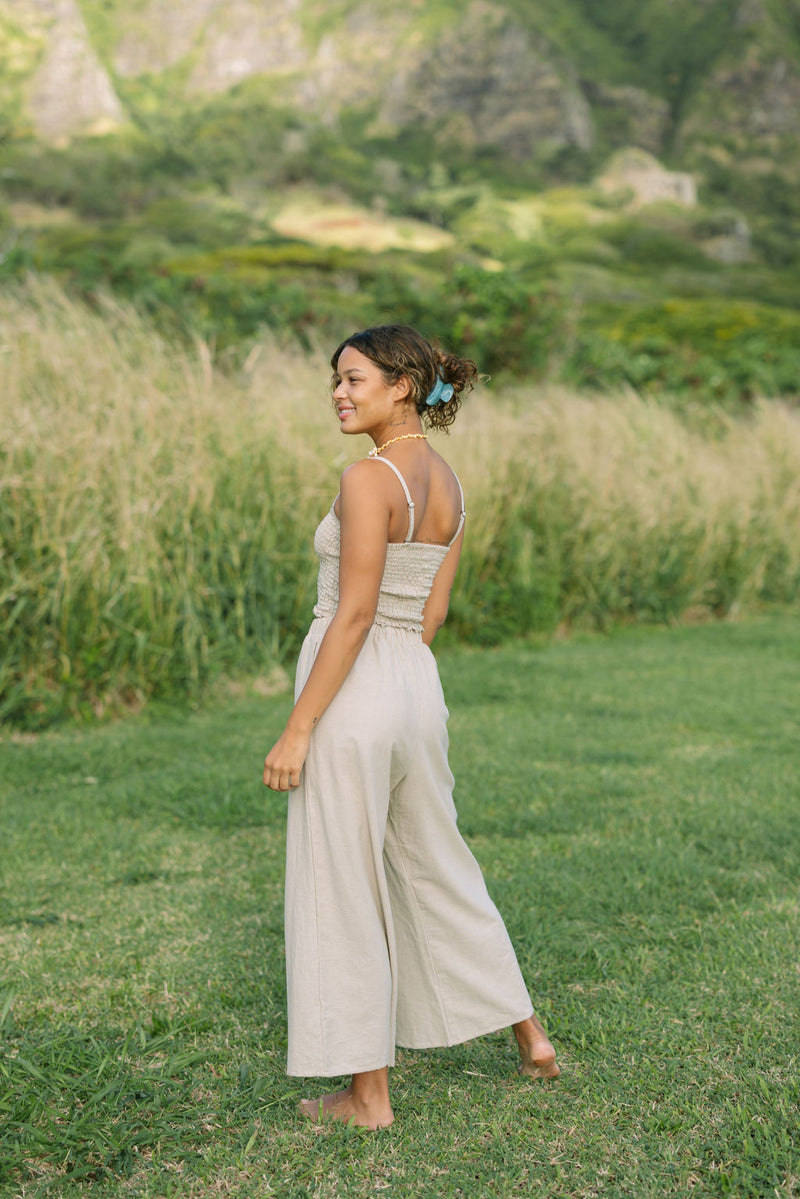 Woman wearing smocked tube top with spaghetti straps and loose pant in beige linen.