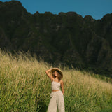 Woman wearing smocked tube top with spaghetti straps and loose pant in beige linen.