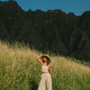 Woman wearing smocked tube top with spaghetti straps and loose pant in beige linen.