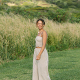 Woman wearing smocked tube top with spaghetti straps and loose pant in beige linen.