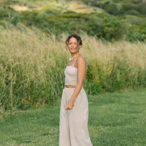 Woman wearing smocked tube top with spaghetti straps and loose pant in beige linen.