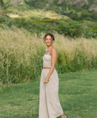 Woman wearing smocked tube top with spaghetti straps and loose pant in beige linen.