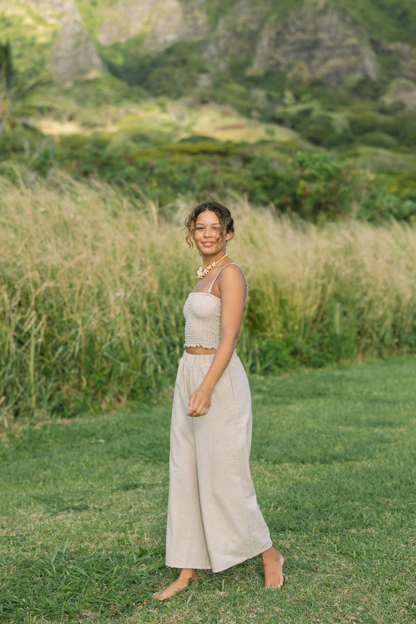 Woman wearing smocked tube top with spaghetti straps and loose pant in beige linen.