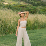 Woman wearing smocked tube top with spaghetti straps and loose pant in beige linen.