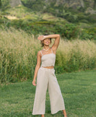 Woman wearing smocked tube top with spaghetti straps and loose pant in beige linen.