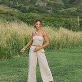 Woman wearing smocked tube top with spaghetti straps and loose pant in beige linen.