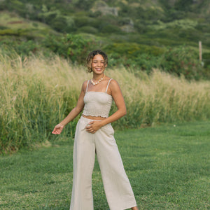 Woman wearing smocked tube top with spaghetti straps and loose pant in beige linen.