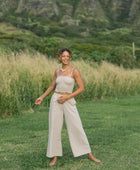 Woman wearing smocked tube top with spaghetti straps and loose pant in beige linen.