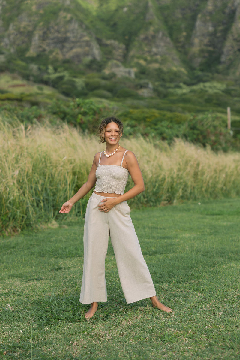 Woman wearing smocked tube top with spaghetti straps and loose pant in beige linen.