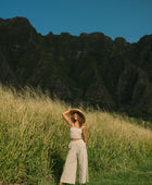 Woman wearing smocked tube top with spaghetti straps and loose pant in beige linen.