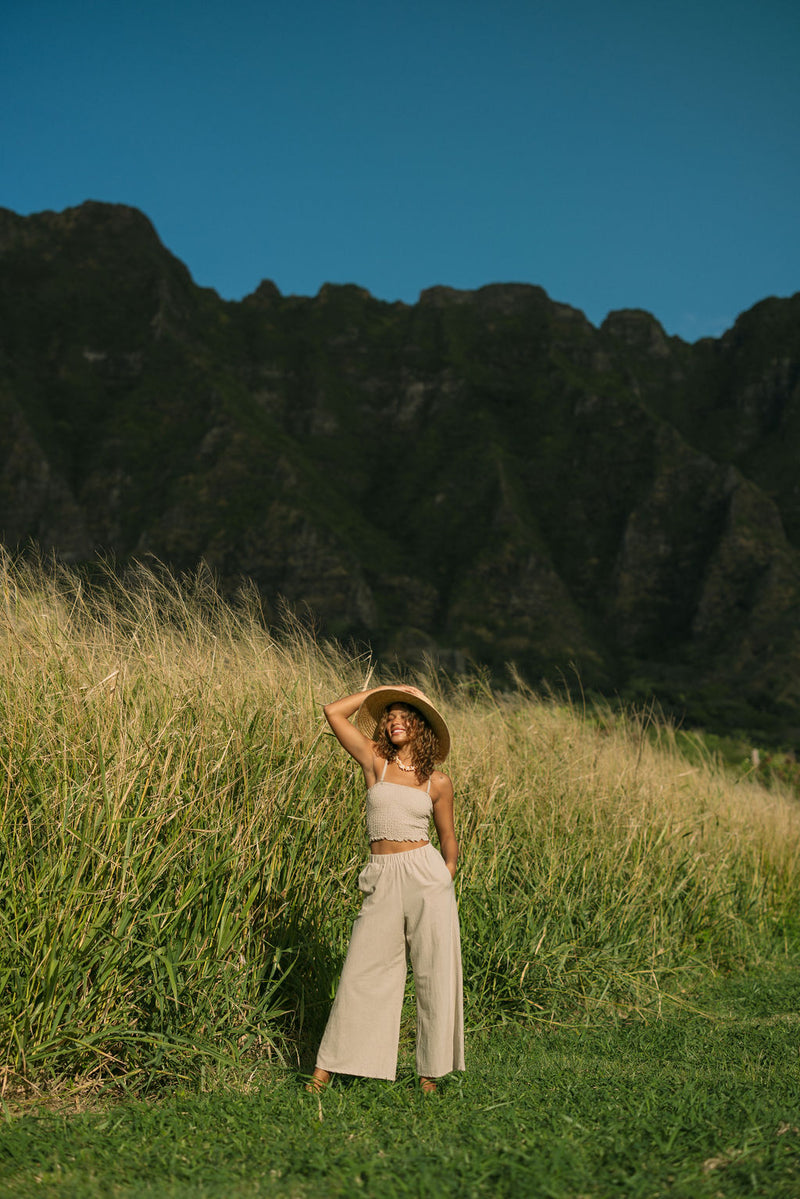 Woman wearing smocked tube top with spaghetti straps and loose pant in beige linen.