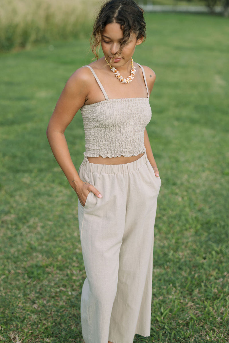 Woman wearing smocked beige linen tube top with spaghetti straps and pant.