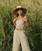 Woman wearing smocked tube top with spaghetti straps and loose pant in beige linen.