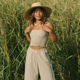 Woman wearing smocked beige linen tube top with spaghetti straps and pant.