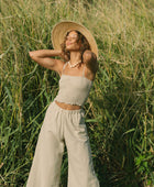 Woman wearing smocked tube top with spaghetti straps and loose pant in beige linen.