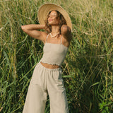 Woman wearing smocked beige linen tube top with spaghetti straps and pant.