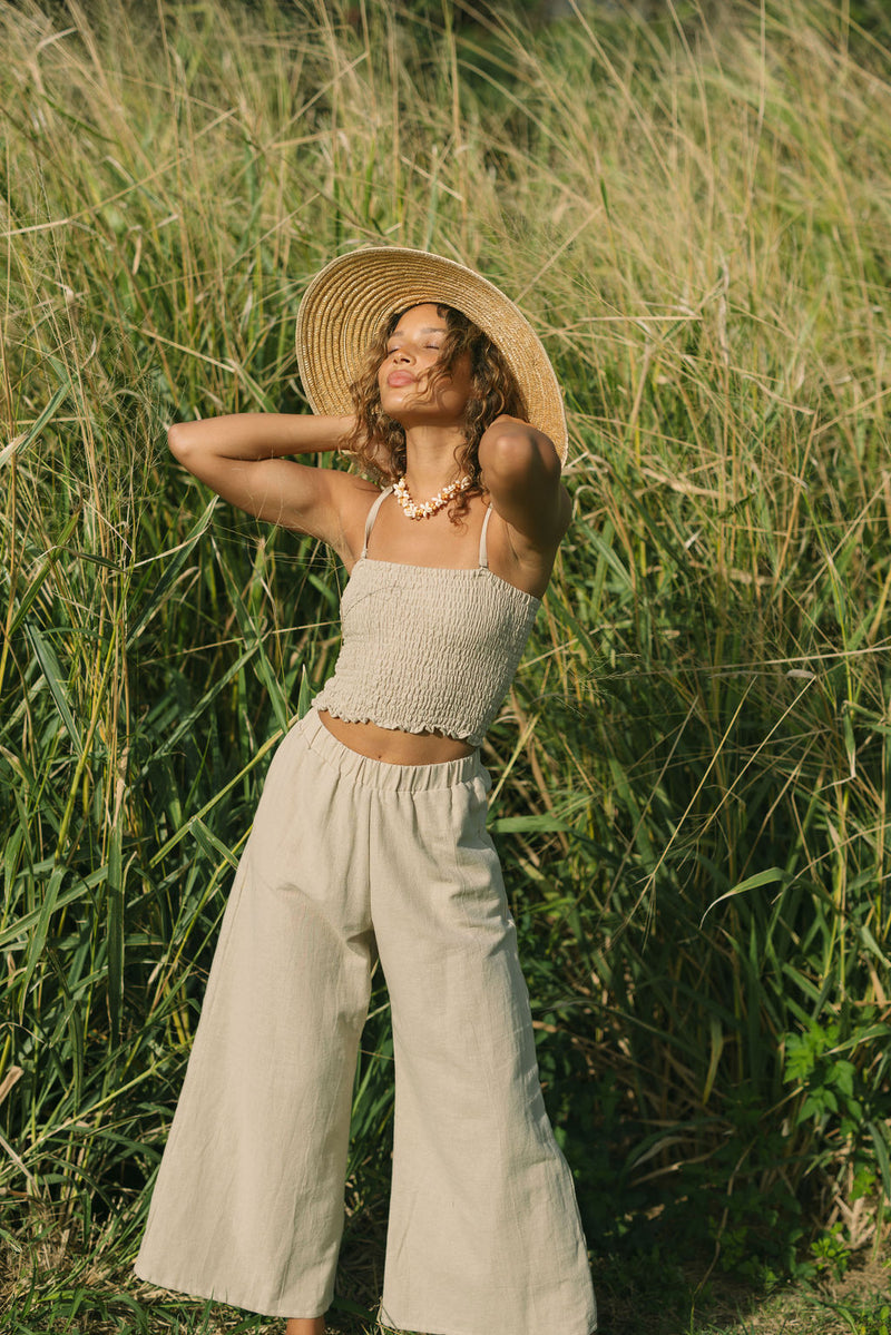 Woman wearing smocked beige linen tube top with spaghetti straps and pant.