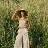 Woman wearing smocked tube top with spaghetti straps and loose pant in beige linen.