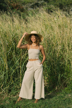 Woman wearing smocked tube top with spaghetti straps and loose pant in beige linen.
