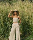 Woman wearing smocked tube top with spaghetti straps and loose pant in beige linen.