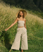 Woman wearing smocked tube top with spaghetti straps and loose pant in beige linen.