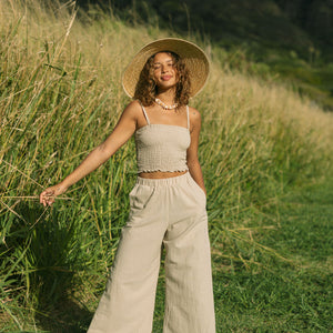Woman wearing smocked beige linen tube top with spaghetti straps and pant.