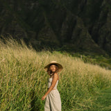 Woman wearing smocked tube top with spaghetti straps and loose pant in beige linen.