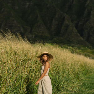 Woman wearing smocked tube top with spaghetti straps and loose pant in beige linen.