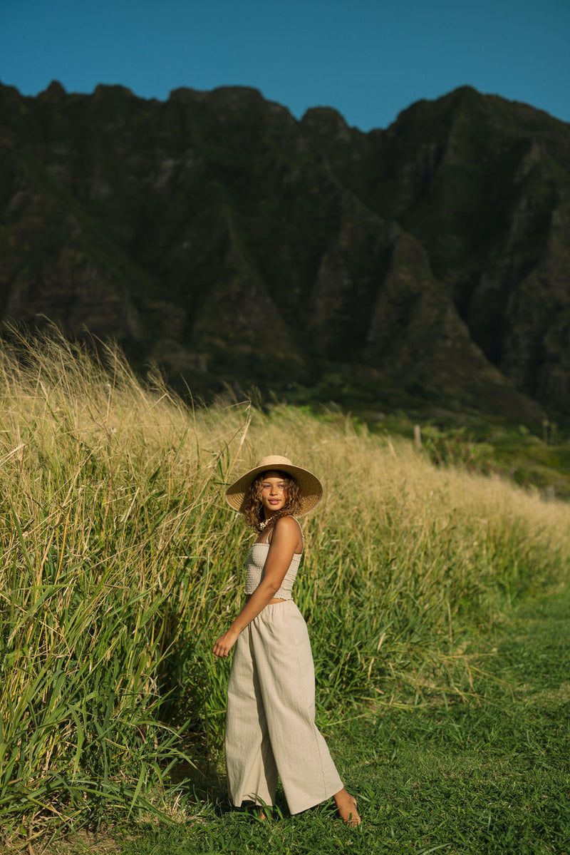 Woman wearing smocked tube top with spaghetti straps and loose pant in beige linen.