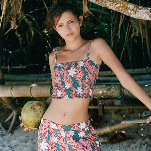 woman with brown hair wearing a bandeau top with removable straps with red ginger and white tiare print