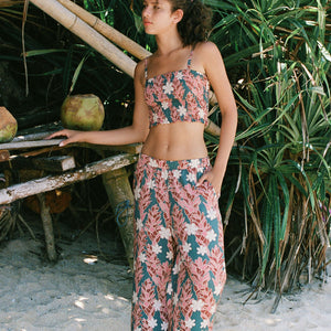 woman with brown hair wearing an elastic waist flowy pant with red ginger and white tiare print