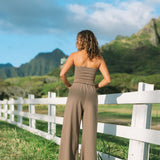 Woman wearing smocked tube top and loose pant in medium brown linen.